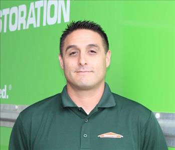 Dark hair technician standing in front of green box truck