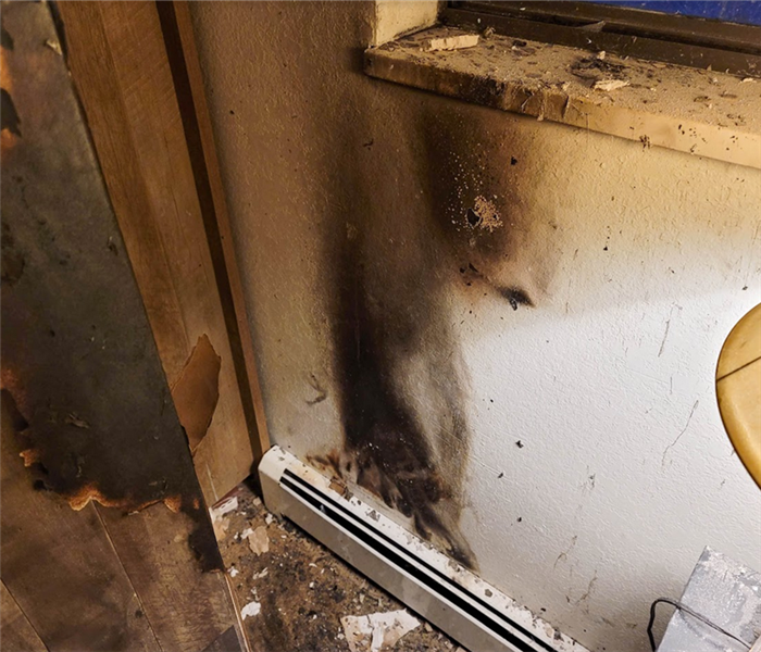a fire damaged wall in a house with debris on the floor and windowsill